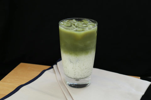 Refreshing iced matcha latte in a glass with milk on a wooden table.