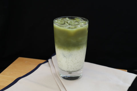 Refreshing iced matcha latte in a glass with milk on a wooden table.