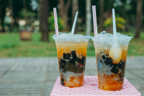 Two iced beverages with toppings in plastic cups sitting outdoors on a pink table.