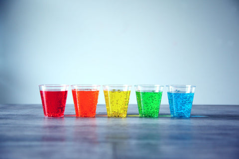 Five colorful fizzy drinks in plastic cups organized in a row indoors.