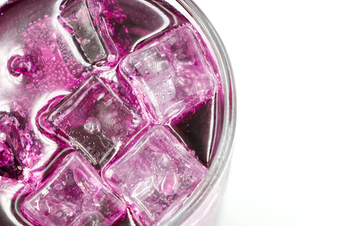 A vibrant pink drink with ice cubes in a glass on a white background.