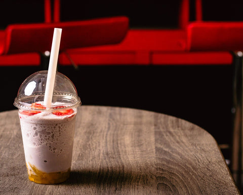 Delicious strawberry milkshake with a straw in a clear cup on a rustic wooden table, perfect for a summer treat.
