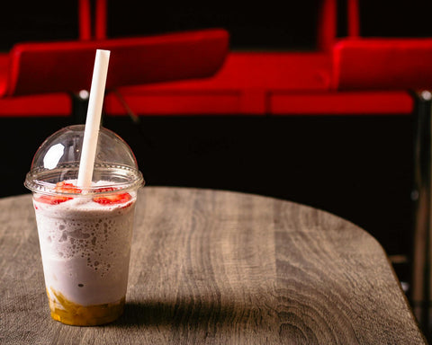 Delicious strawberry milkshake with a straw in a clear cup on a rustic wooden table, perfect for a summer treat.