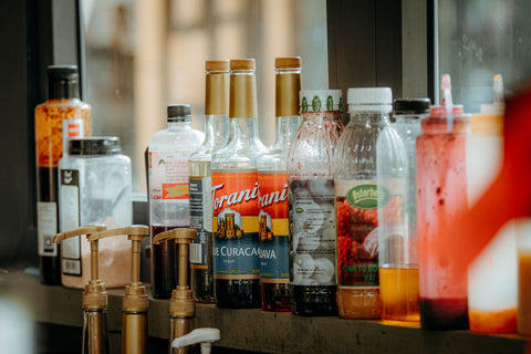 A variety of bottles including syrups and condiments on a café counter.