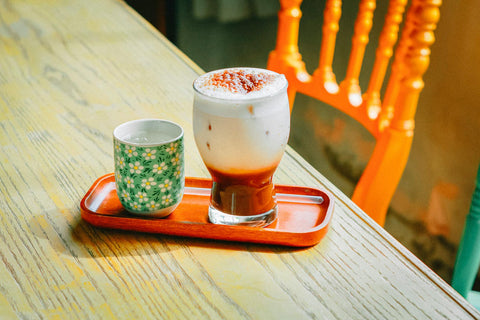 A cozy scene featuring an iced latte and tea cup on a wooden table with orange chair.