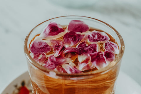 A refreshing glass of iced tea topped with vibrant pink rose petals, perfect for a summer beverage.