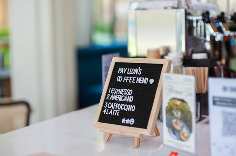 A wooden menu board in a coffee shop displaying espresso varieties like Americano and Latte.