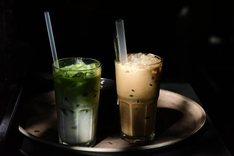Close-up of iced matcha latte and brown sugar milk tea served in glasses with straws.