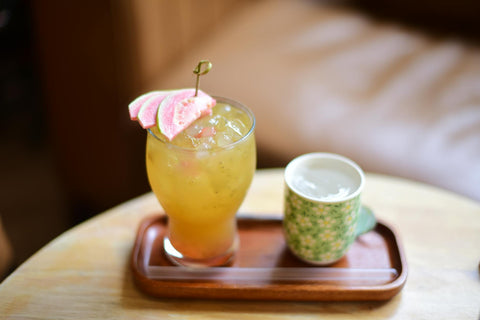 A vibrant guava cocktail and tea cup on a wooden tray, perfect for a cozy indoor setting.