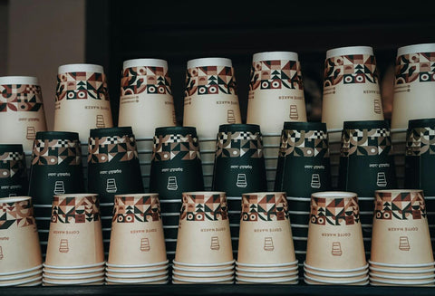 Colorful stack of paper coffee cups with geometric patterns in a cafe setting.