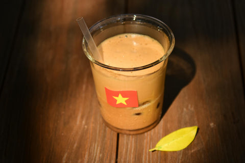 Glass of Vietnamese iced coffee with flag sticker on a wooden table.