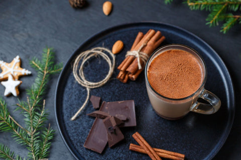 A warm glass of cocoa surrounded by cinnamon sticks, chocolate, and festive cookies.