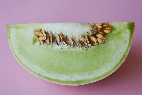 Piece of ripe juicy sweet melon with small seeds placed on pink background