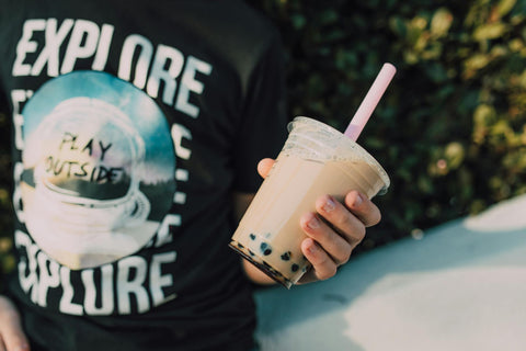 Close-up of a person holding delicious bubble tea outdoors, with vibrant surroundings.