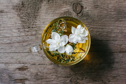Top view of fresh white Arabian jasmine flowers in glass cup of aromatic herbal tea served on wooden table in kitchen