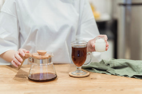 A close-up of a person preparing herbal tea with milk in a cozy indoor setting.