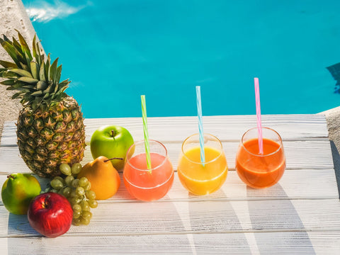 Colorful tropical drinks and fruits by a swimming pool, perfect for summer refreshment.