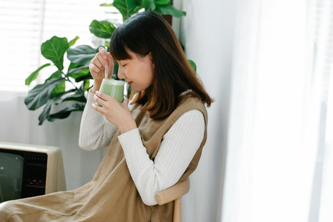 A relaxed Asian woman savoring a warm matcha latte in a cozy indoor setting.