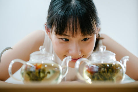 Close-up of a smiling woman appreciating tea in clear glass teapots indoors.