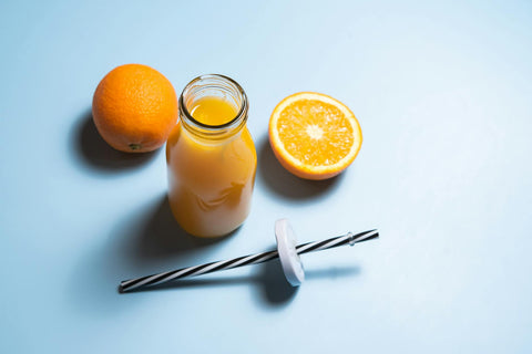 Top view of fresh orange juice in a bottle with whole and sliced oranges on a light blue background.