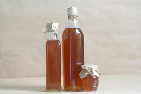 Still life composition of glass bottles and a jar filled with honey, emphasizing rustic charm.