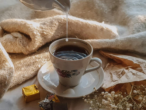 A cozy fall setup with a cup of coffee being poured with milk, surrounded by warm tones and textures.